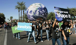 Students marching in homecoming parade carrying signs promoting sustainability and a big globe of the earth.